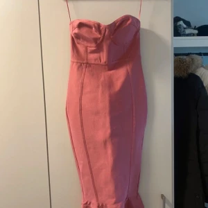 Rosa axelbandslös klänning - Säljer en superfin rosa axelbandslös klänning med en tight passform. Klänningen har en dragkedja bak och en söt volangdetalj längst ner. Perfekt för fest eller sommarens alla tillfällen! 💖