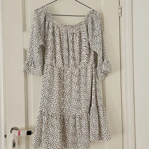 Vit och svart prickig klänning - Säljer en superfin vit klänning med svarta prickar. Den har trekvartsärm och en söt volangdetalj vid ärmslut och nederkant. Perfekt för sommarens alla fester eller en mysig dag på stan. Klänningen har en bekväm passform och är gjord i ett lätt material.