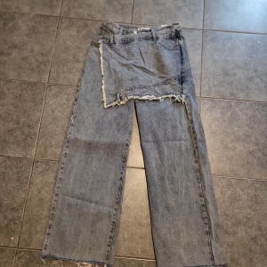 Unika jeans med fransiga detaljer - Säljer ett par unika jeans med fransiga detaljer och en cool, asymmetrisk design. De är i en klassisk blå jeansfärg och har en loose passform. Perfekta för dig som vill sticka ut med en edgy stil. Tillverkade i Korea. om ni vill se bild på skriv :)