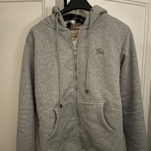 Burberry hoddie  - Säljer en grå Burberry zip hoodie i storlek S. Hoodie är i bra skick och av hög kvalitet, perfekt för den som gillar stil och komfort. Klassisk design med Burberrys ikoniska detaljer.  Skicka PM INNAN ni köper!
