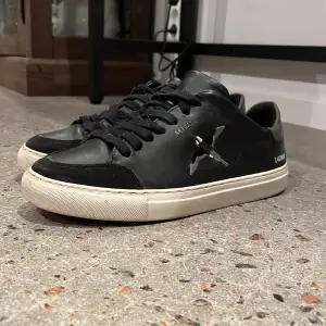 Säljer ett par snygga svarta sneakers från Axel arigato med vit sula. Skorna är i skinn och har snörning. Perfekta för vardagsbruk och ger en stilren look. Nypris:2400