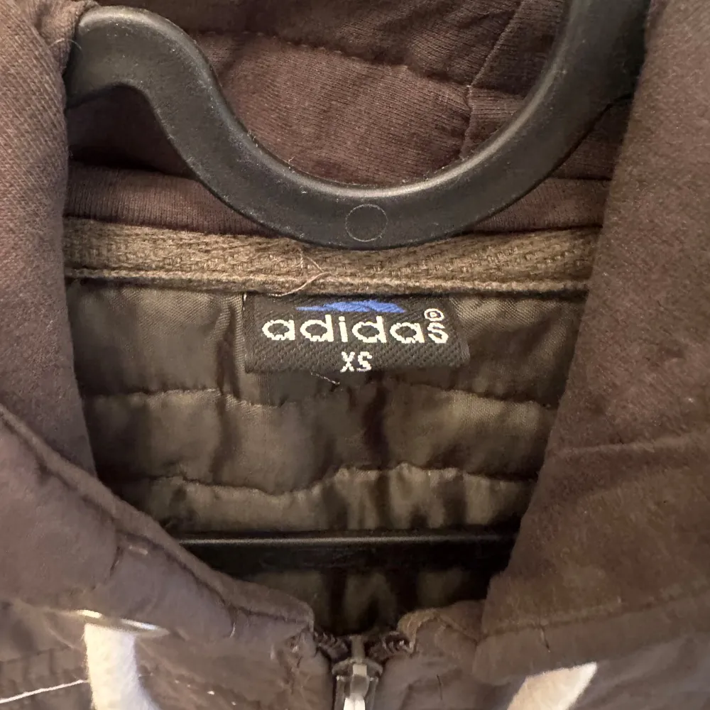 Säljer en snygg svart jacka från Adidas. Den har en dragkedja framtill och vita detaljer som de klassiska Adidas-ränderna på ärmarna. Jackan har en huva med vita snören och två fickor med dragkedja. Perfekt för höst och vår! XS. Jackor.