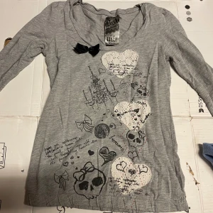 Grå långärmad tröja med tryck och spetsdetaljer - Fin grå långärmad tröja från Berskha. Har ett tryck med hjärtan, dödskallar och en ljuskrona. Perfekt för höst och vinter!