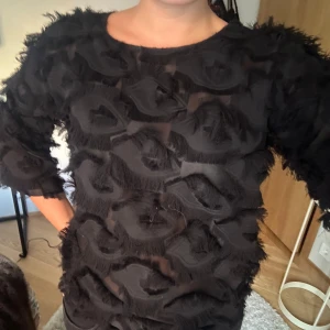 Svart topp från Twist & Tango - Säljer en supercool svart topp från Twist & Tango. Den har ett unikt mönster med fransiga detaljer som ger en snygg textur. Toppen är perfekt för en utekväll eller fest och har trekvartsärmar. 