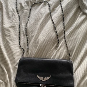 Zadig & Voltaire väska  - Väskan är använd men i väldigt fint skick, det är 1 sten borta på ”vingen”. Vingarna sitter ytterst lite löst i kanterna men inget av ovan syns om man ej kollar nära 💞 dustbag har tyvärr slängts. Skriv för fler frågor el bilder. Nypris 3600 kr.