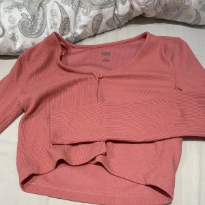 Rosa ribbad kofta från 157 - Säljer en superfin rosa ribbad kofta från 157. Den har en enkel knapp framtill och är perfekt för både vardag och fest. Koftan är i storlek S och har långa ärmar. Den är i nyskick och redo för en ny garderob!