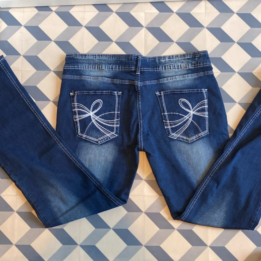 Säljer ett par snygga lågmidjade blå jeans med coola broderade detaljer på bakfickorna. De har en klassisk femficksdesign och en knapp- och dragkedjestängning framtill. Perfekta för både vardag och fest!. Jeans & Byxor.