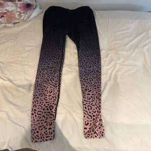 Svarta och rosa leggings med leopardmönster från Iconic - Säljer ett par snygga träningsbyxor från Iconic i storlek 158/164. De är svarta upptill och övergår till rosa nedtill med ett coolt leopardmönster. 