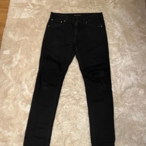 Svarta jeans från Nudie Jeans - Snygga svarta jeans från Nudie Jeans med klassisk design. De har en normal passform och är tillverkade i ett slitstarkt material. Perfekta för en stilren look. Amvdända 2-3 gånger och har inga defekter.