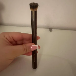 Concealer Sminkborste från Hourglass - Snygg sminkborste från Hourglass med ett elegant brunt handtag och täta, mjuka borst. Perfekt för att applicera foundation eller puder jämnt över ansiktet. Borsten är designad för att ge en felfri finish. Endast använd en gång för att testa den! Ny pris 530 kr!