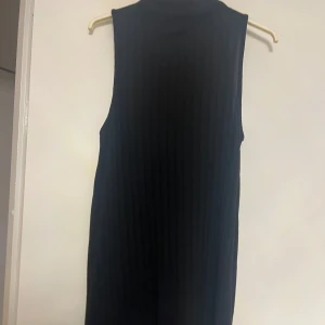 Svart ärmlös ribbad klänning - Snygg svart ärmlös klänning med ribbad struktur. Perfekt för en stilren look. Klänningen har en enkel design som gör den lätt att matcha med olika accessoarer.