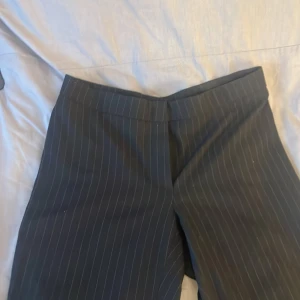 Svarta randiga kostymbyxor - Snygga svarta kostymbyxor med diskreta ränder. Byxorna har en dragkedja och knapp framtill för enkel stängning. Perfekta för en stilren look.