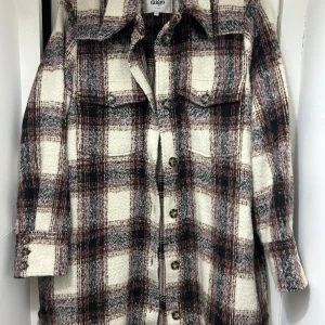 Rutig jacka från Twist & Tango - Säljer en snygg rutig jacka från Twist & Tango i storlek L. Jackan har en klassisk krage och knappar framtill. Den är i en härlig blandning av beige, brun och svart med långa ärmar och fickor på bröstet.