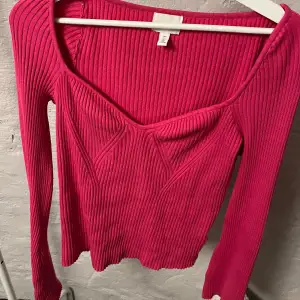 Snygg rosa ribbad tröja från H&M med en unik v-ringad design. Tröjan har långa ärmar och en figurnära passform som framhäver silhuetten. Perfekt för att lägga till en färgklick i garderoben!
