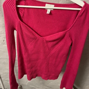 Rosa ribbad tröja - Snygg rosa ribbad tröja från H&M med en unik v-ringad design. Tröjan har långa ärmar och en figurnära passform som framhäver silhuetten. Perfekt för att lägga till en färgklick i garderoben!