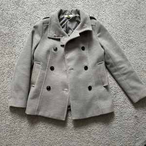Grå kappa från H&M - Snygg grå kappa från H&M med dubbelknäppning och stilrena knappar. Jackan har en klassisk design med långa ärmar och en rak passform. Perfekt för kyligare dagar och ger en elegant touch till din outfit. Storlek 40. Pris går att diskutera vid snabb affär. 😊