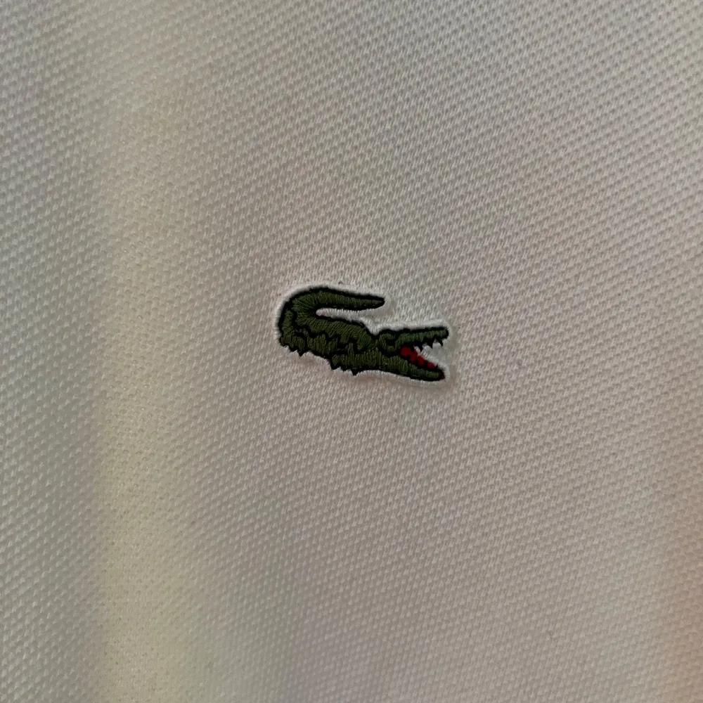 Säljer en klassisk vit pikétröja från Lacoste med den ikoniska krokodilloggan på bröstet. Tröjan har korta ärmar och en stilren krage med knappar. Perfekt för en avslappnad och stilren look. Storlek 4 som sitter som en M. Skick som nytt!. Paidat.