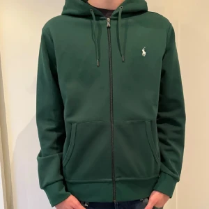 Grön hoodie från Ralph Lauren - Snygg ovanlig grön hoodie från Ralph Lauren med dragkedja och broderad logga på bröstet. Tröjan har en justerbar huva med snören och praktiska fickor framtill. Perfekt för en avslappnad stil. Skriv vid frågor!!!