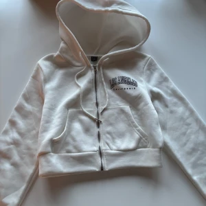 Vit hoodie med Los Angeles-tryck - Vit kort hoodie med dragkedja och tryck 'Los Angeles California' på bröstet. Snygg, men säljer för att den inte är min stil längre🥰 pris kan diskuteras