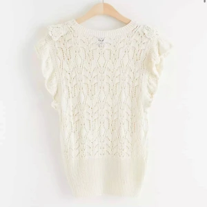 Vit stickad topp från Lindex - Säljer en söt vit stickad topp från Lindex med vackert spetsmönster och volangdetaljer vid ärmarna. Toppen är ärmlös och har en ribbad nederkant för en fin passform. Inga defekter.