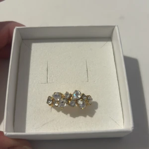 Guldfärgad ring med glittriga stenar - Elegant guldfärgad ring prydd med flera glittriga stenar i en vacker formation. Perfekt för att ge en touch av glamour till din outfit. Justerbar storlek för att passa de flesta fingrar.