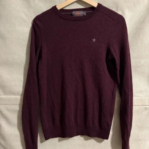 Vinröd ulltröja från Morris - Säljer en stilren vinröd tröja från Morris i 100% merinoull. Tröjan har en liten broderad detalj på bröstet och ribbade kanter vid ärmslut och nederkant. Perfekt för kyligare dagar.