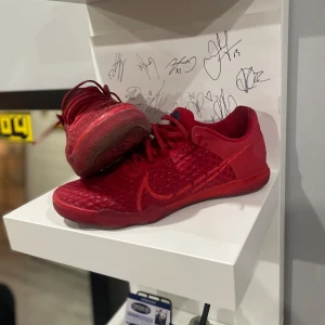 Röda Nike inomhusskor  - Snygga röda Nike sneakers med en unik textur och snörning. Skorna har en distinkt sula med cirkulära mönster för bra grepp. Perfekta för en sportig look.