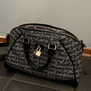 Mönstrad väska från Juicy Couture - Jag har köpt den från Usa och den är äkta. Den är knappt använd. Snygg väska från Juicy Couture med ett iögonfallande mönster i svart och beige. Väskan har dubbla handtag och en avtagbar axelrem för flexibilitet. Den är försedd med en dragkedja och ett dekorativt lås framtill. Perfekt för att ge din outfit en trendig touch!  