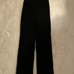 Svarta ribbade byxor - Snygga svarta byxor med ribbad struktur och hög midja. De har en loose passform och är perfekta för en avslappnad stil. Byxorna är tillverkade i ett mjukt material som ger en bekväm känsla hela dagen.