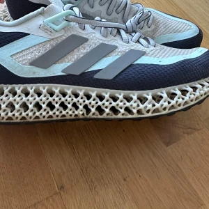 Adidas 4DFWD 2 Dam - Säljer ett par Adidas 4DFWD 2 sneakers i en stilren kombination av ljusblått och grått. Skorna har en unik 3D-printad sula som ger extra komfort och stöd. Perfekta för både träning och vardag. Snörning framtill för justerbar passform. Använd några gånger. Storlek 41 1/3