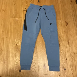 Blå Nike tech fleece mjukisbyxor - Snygga blå mjukisbyxor från Nike med svarta detaljer. Byxorna har en bekväm passform med resår i midjan och snörning för justering. Perfekta för en avslappnad stil. Pris kan diskuteras om köpta med hoodien i min profil