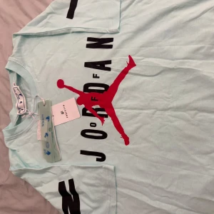 Ljusblå t-shirt med Jordan-tryck - Säljer en ljusblå t-shirt med ett stort rött Jordan-tryck på framsidan och svart text. T-shirten har korta ärmar och är i en skön bomullskvalitet. Perfekt för en avslappnad stil. Lite dyrare då det är collad med off white men billig för vill bli av med den!