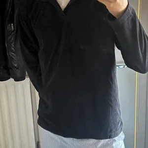 Svart långärmad Frottétröja - Säljer en stilren svart långärmad tröja med krage. Perfekt för en avslappnad look. Tröjan har en enkel design utan mönster eller detaljer.