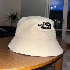 Beige hatt från The North Face - Snygg beige hatt från The North Face med broderad logga i svart. Perfekt för en avslappnad stil och skydd mot solen. Hatten har en klassisk design.