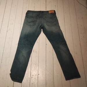 Blå jeans från Jack & Jones - Snygga blå jeans från Jack & Jones med slitna detaljer och en klassisk femficksdesign. Perfekta för en avslappnad stil. Märkeslapp baktill och knappgylf framtill.