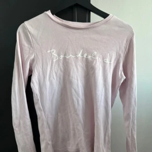 Ljusrosa långärmad tröja från Bondelid - Säljer en ljusrosa långärmad tröja från Bondelid med tryckt logga på framsidan. Perfekt för en avslappnad stil. Tröjan är i en mjuk och bekväm bomullskvalitet.
