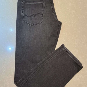 Grå jeans från Jack & Jones - Snygga grå jeans från Jack & Jones med en klassisk femficksdesign. De har en rak passform och är tillverkade i ett bekvämt denimtyg. Perfekta för en stilren look. Köpte dem och tog av etiketterna sedan efter när jag skulle sätta på mig dem så märkte jag att dem var för små annars helt nya!