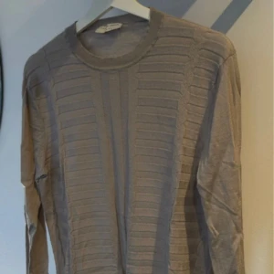 Beige tröja från Tiger of Sweden - Säljer en stilren beige tröja från Tiger of Sweden. Tröjan har ett diskret ribbat mönster och långa ärmar. Perfekt för en elegant och avslappnad look.