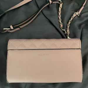 Rosa don Donna väska💗 - Säljer nu denna väska från don Donna som jag köpte för cirka 2 år sedan men som tyvärr aldrig kommit till andvändning. Den kan både bli buren som en axelremsväska eller om man knäpper av banden kan man bära den som en clutch väska❤️ skriv för mer detaljer eller bilder🥰