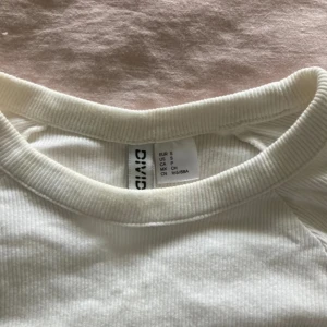 Vit ribbad topp - Säljer en stilren vit ribbad topp från Divided. Toppen har korta ärmar och en rund halsringning, perfekt för en enkel och snygg look. Passar bra till både jeans och kjol. Hör av dig vid intresse! 🤍