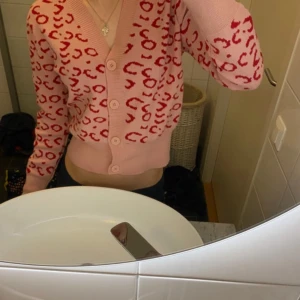 Rosa leopardmönstrad kofta - Säljer en söt rosa kofta från QED London med leopardmönster i rött. Koftan har en v-ringad design med knappar framtill och långa ärmar. Perfekt för att lägga till en färgglad touch till din outfit! 🐆