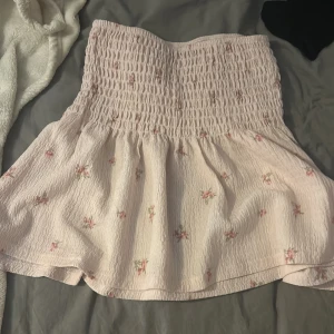 Ljusrosa blommig kjol från Gina Tricot - Söt ljusrosa kjol från Gina Tricot med ett blommigt mönster. Kjolen har en smockad midja som ger en bekväm passform och en lätt utsvängd form. Perfekt för en somrig look! 🌸har inte använt!