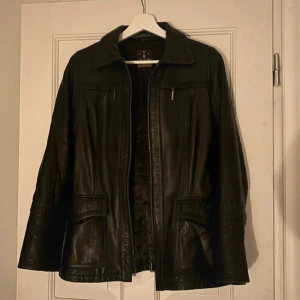 Snygg vintage skinnjacka  - Snygg svart skinnjacka från R&R med dragkedja framtill och flera praktiska fickor. Jackan har en klassisk krage och långa ärmar. 
