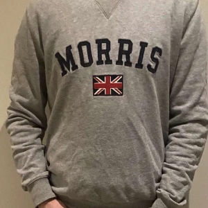 Grå sweatshirt från Morris - Säljer en stilren grå sweatshirt från Morris med ett broderat brittiskt flaggmotiv och texten 'Morris' på framsidan. Tröjan har långa ärmar och ribbade muddar vid ärmslut och nederkant. Perfekt för en avslappnad stil. Inga defekter om ni har färgar är de bara att höra av sig priset är diskuterbart vid snabb affär! 