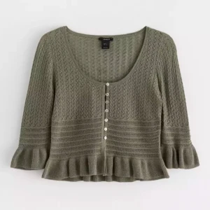 Olivgrön stickad kofta med volang - Säljer en olivgrön stickad kofta från lindex med vacker spetsstickning och knappar framtill. Koftan har trekvartsärmar och en söt volangdetalj vid ärmslut och nederkant. Perfekt för en stilren och mysig look.