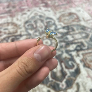 Guldfärgad ring med blå sten - Elegant guldfärgad fidget spinner med en vacker blå sten i form av en fjäril. Perfekt folk med stress och pilar mycket på naglar. Istället för att pila på naglarna så kan du istället snurra på fjärilen som en fidget spinner.