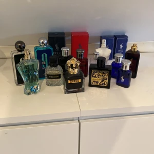 Samling av herrparfymer - En samling av olika herrparfymer med varierande design och färger. Inkluderar flaskor i blått, svart och genomskinligt glas med detaljer i silver och guld. Märken som syns är bland annat Polo och Valentino. Perfekt för den som vill ha ett brett urval av dofter.