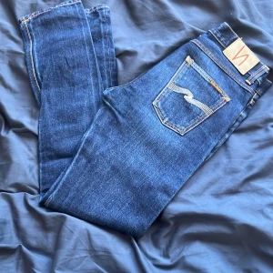 Mörkblå nudie jeans - Säljer ett par mörkblå nudie jeans i bra skick. De har en slim passform och är perfekta för både vardag och fest. Klassisk design med fem fickor och knappgylf. Passar till det mesta i garderoben!