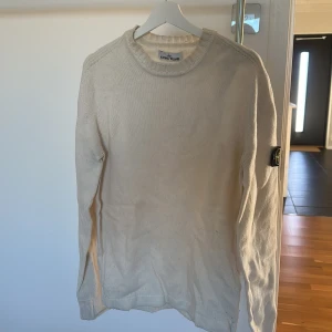 Vit tröja från Stone Island - Säljer en stilren vit tröja från Stone Island. Tröjan har långa ärmar och en rund halsringning. Perfekt för en avslappnad och trendig look. Märkeslogga på ärmen ger en extra touch av stil. Behöver sig en tvätt då jag inte använt den på flera år.