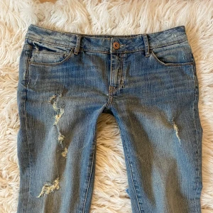 Låg midjade blå bootcut jeans med slitningar - Säljer även ett par lågmidjade jeanshorts! Supersnygga och coola lågmidjade bootcut jeans med slitningar som tyvärr är  för stora för mig! Midja rakt över: ca 41-42 cm, innerben: ca 84 cm (pytteliten defekt finns, skriv för bild på den men den märks knappt)💞